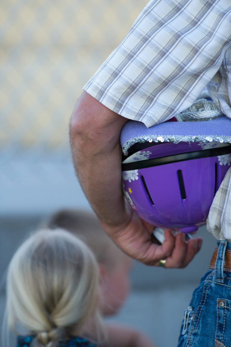 father holding childs purple horse riding helmet under arm with