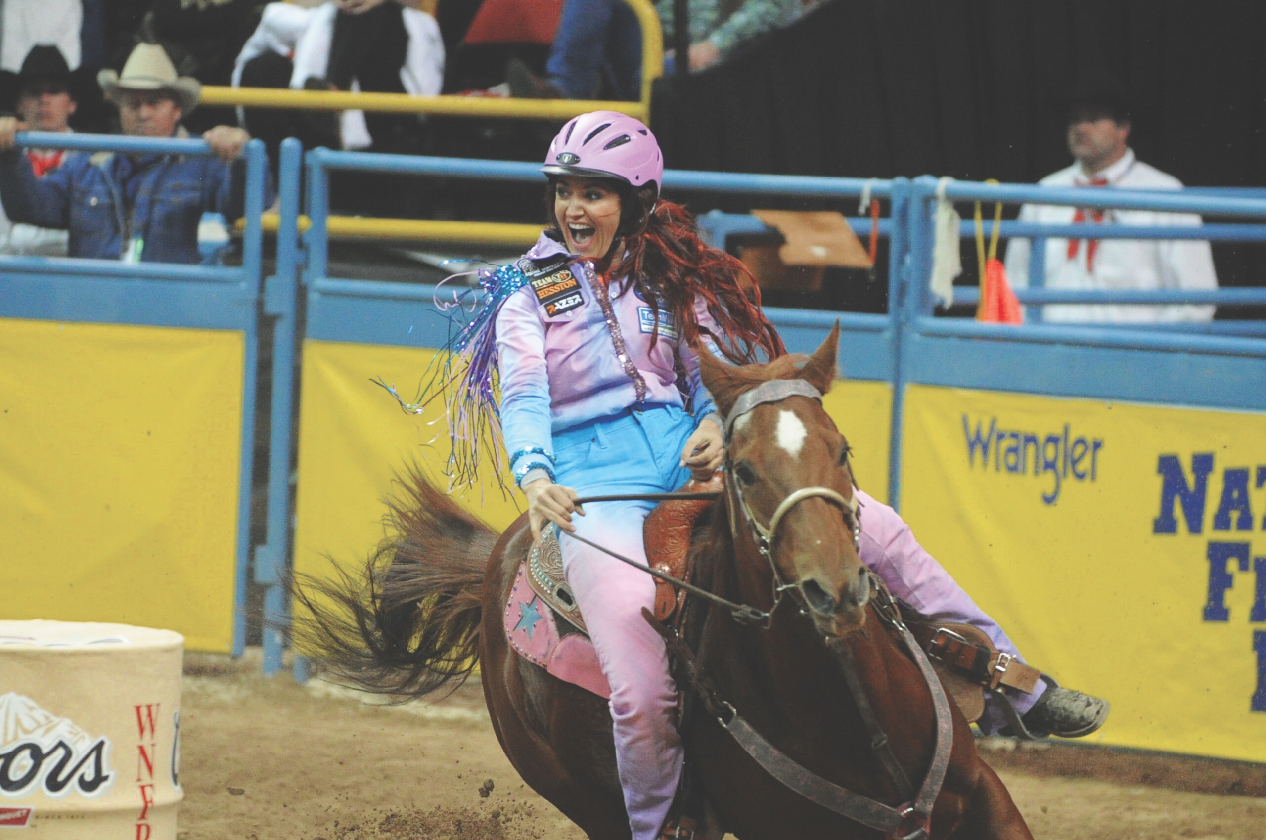 Barrel racing world champion Fallon Taylor smiles as she rounds a barrel in a pink outfit at the rodeo