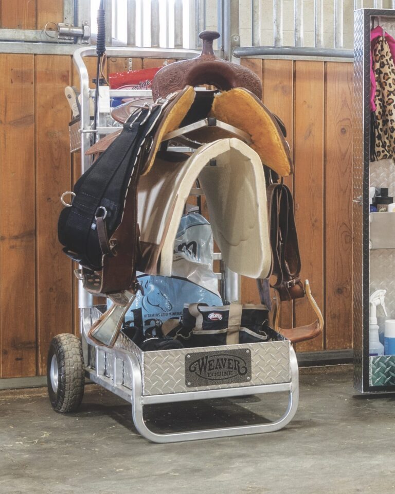 Weaver Equine Rolling Barn Utility Cart loaded with a saddle, pads, feed, and grooming gear in a horse barn aisle.