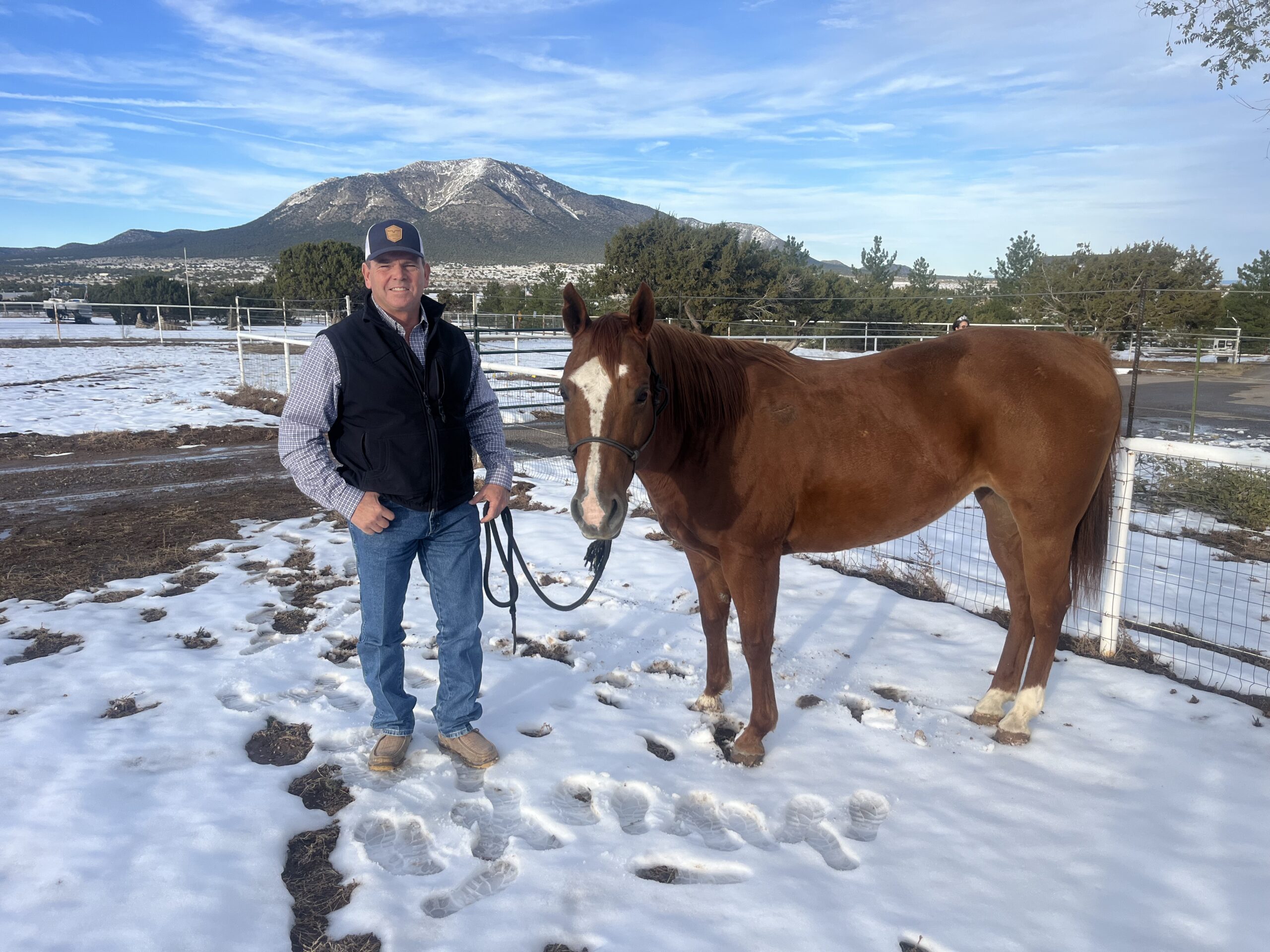Bill Norman stands with his sorrel horse, Jessie, in a snowy paddock below a mountain.