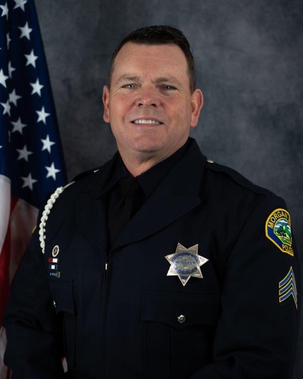 Bill Norman in a Morgan Hill Police Department uniform in front of an American flag.