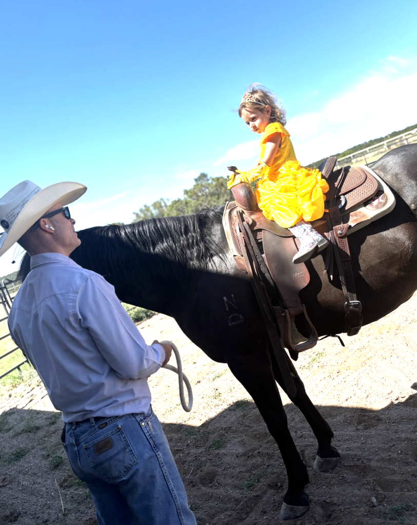 Lettie, dressed as Belle from "Beauty and the Beast," sits on a dark horse as a her dad, Jeremy Svejcar, wearing a cowboy hat, holds the lead rope.